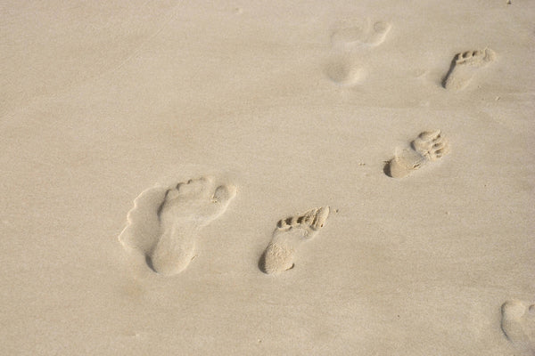 Footprints of an adult and child on the beach.