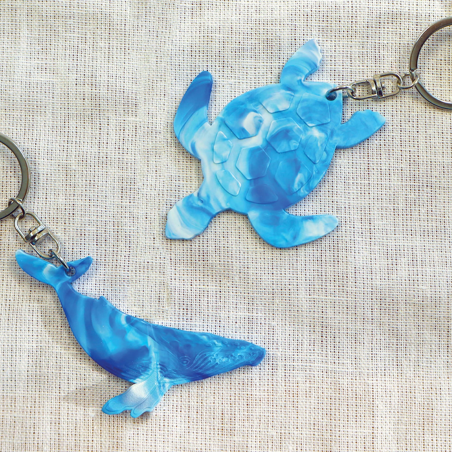 Blue and white bag tags made with recycled plastic milk bottle lids, in the shape of a turtle and humpback whale.