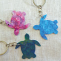 Purple, blue and green turtle shaped keyrings made with recycled plastic milk bottle lids.